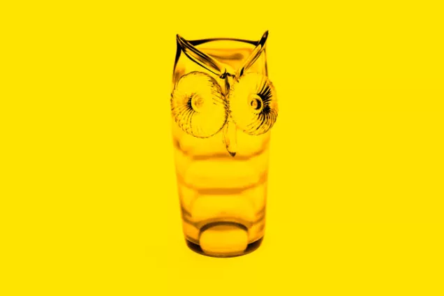 ett uggleformat glas mot gul bakgrund.
