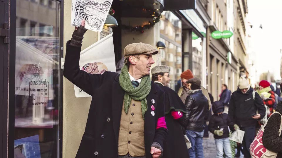 Man i gammaldags kläder säljer en tidning på en gata. Foto. 