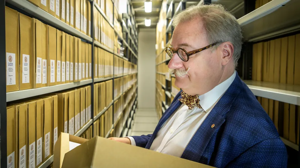 Man tittar i handlingar bland hyllor. Foto.