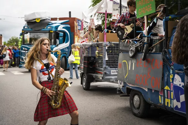 Kvinna spelar saxofin i kilt framför en karnevalsvagn. 
