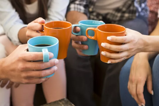 Fyra personers händer håller i kaffekoppar.