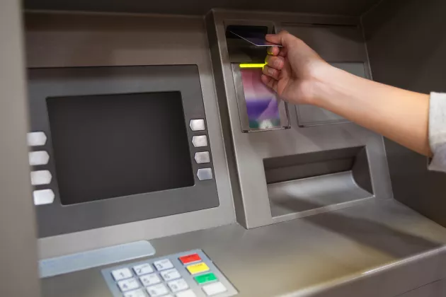 Hand som stoppar in ett kreditkort i en bankomat.
