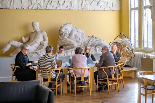 Flera personer sitter runt ett bord och samtalar omgivna av statyer på Pufendorfinstitutet. 