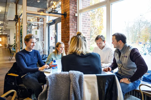 ett antal studenter sitter och diskuterar i ett bibliotek.