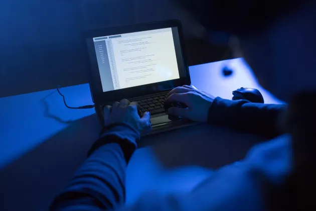 Händer på ett tangentbord i ett mörkt rum.