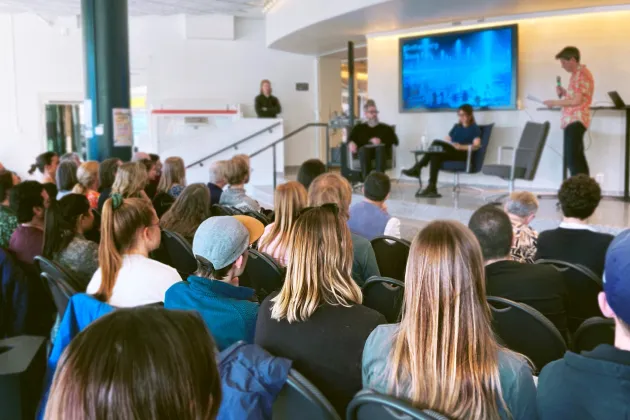 Tre personer sitter på en scen med en publik framför sig.