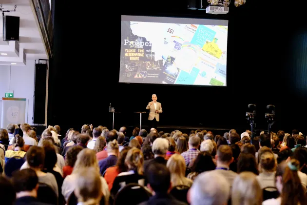 En stor publik framför en scen med en Tv-skärm och en talare.
