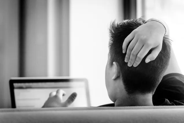 Man som sitter och gestikulerar framför en datorskärm. Sett bakifrån. Foto.