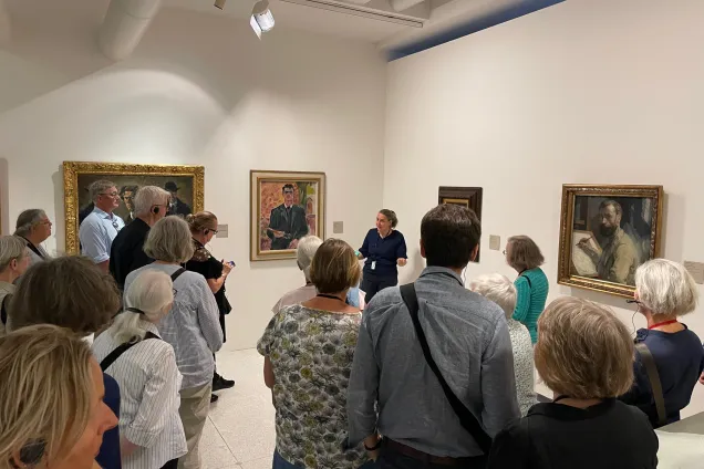 Foto av människor som står på en konsthall och får en guidning.