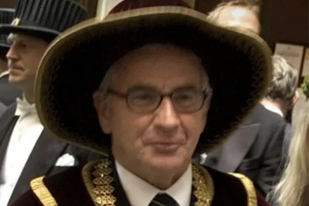 Man i rektorsutstyrsel, hatt och glasögon.