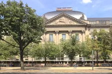 Foto av fasaden på Staatsbibliothek zu Berlin. Träd och grönska i förgrunden.