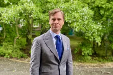 En man poserar framför ett grönområde.