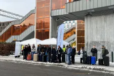 En massa människor som står i snö och väntar vid en busshållplats.