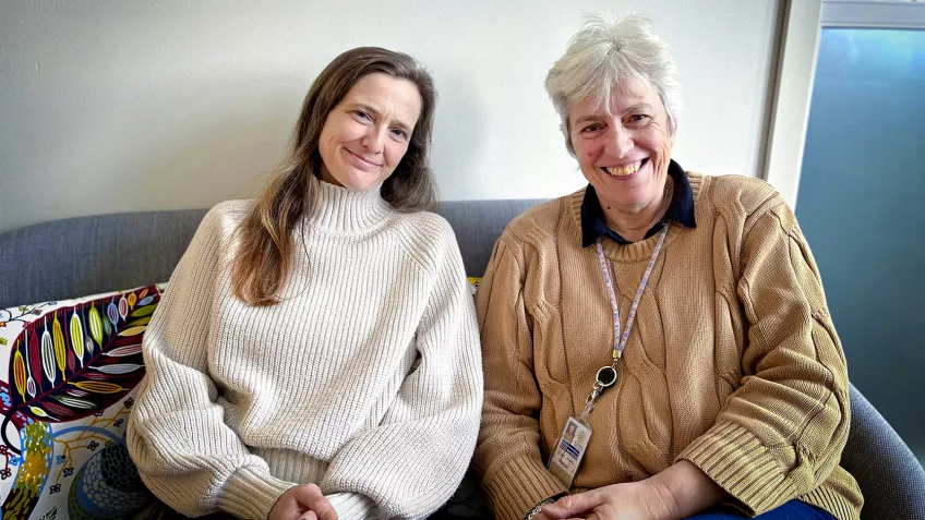 Foto på Lena Christensen och Rachel Forsyth som sitter i en soffa och leende tittar in i kameran. 