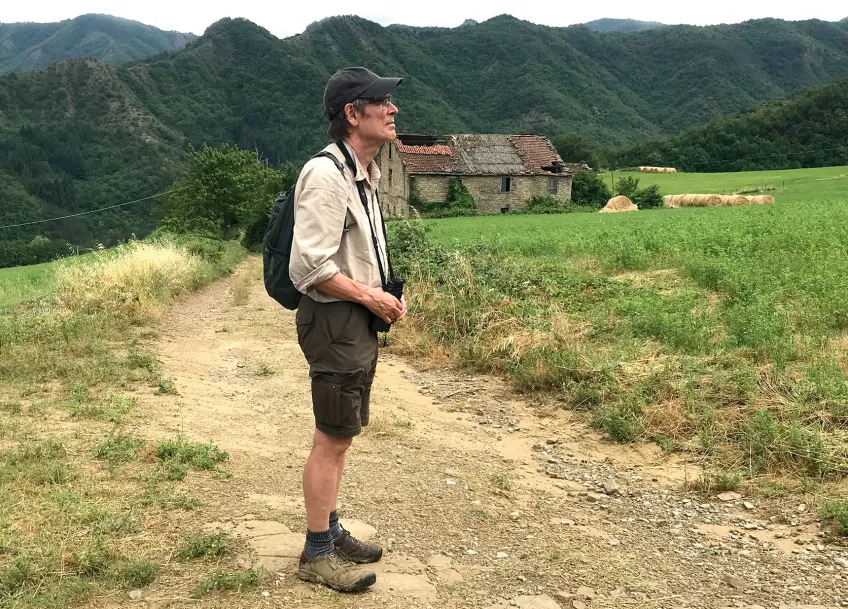 Man i shorts och skjorta blickar ut över ett kuperat landskap. foto