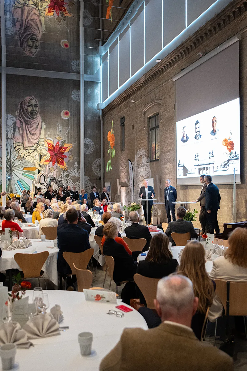 Många människor som sitter vid fint dukade bord i en stor sal.